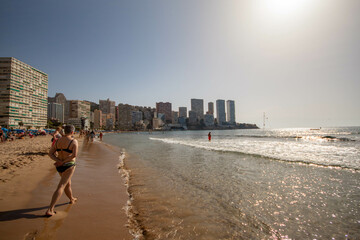 Personas caminando por la orilla de la playa de Benidorm en bañador bajo un precioso día soleado...