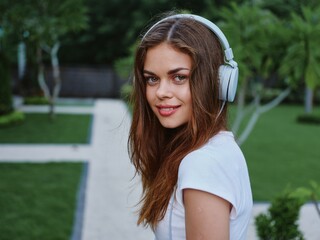 Woman wearing headphones looks into camera and listens to music while traveling in Asia