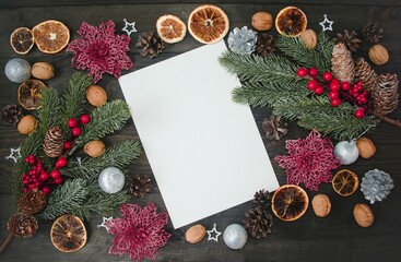 Fototapeta na wymiar On a wooden background a white sheet of paper for copying text. The concept of a New Year's atmosphere, Christmas decorations, cones, oranges, fir branches, shiny flowers. Concept of Christmas. 