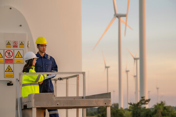 Two engineers working and holding the report at wind turbine farm Power Generator Station on mountain,Thailand people,Technician man and woman discuss about work