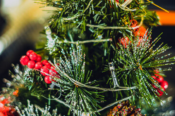 Christmas tree artificial decorative plastic green shiny sequins sprinkles, LED garland light, red berry ball rowan tassels. Winter holiday leisure. Bright