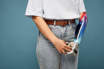 Cropped image of woman with prosthetic arm standing against blue background