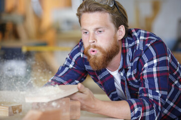 male carpenter blowing wood shavings in workshop