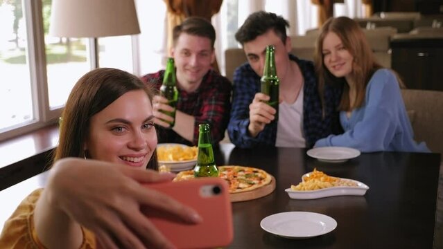 A group of cheerful friends relax in a cafe, eat pizza and chips, drink beer and take selfies. Friends are photographed as a memento of a meeting in a pizzeria. Meeting old friends.