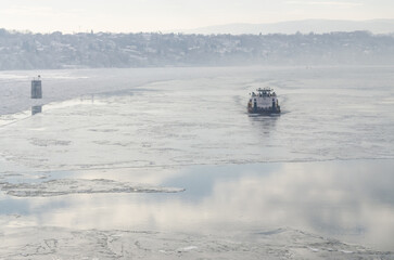 The bank of the Danube river covered with snow. Danube River covered with snow and ice. An icebreaker ship in the frozen and snow-covered waterway of the Danube River below the Petrovaradin Fortress, 