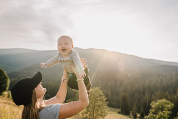 The mother throws up his happy son into the sky with his hands. Walking in nature on an autumn day. Mom and baby child playing in the mountains. Concept of family spending time together on vacation.
