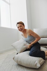 Teenage girl smile everyone sits at home near the couch and tosses up pillows, fun game and happiness without filters, copy place