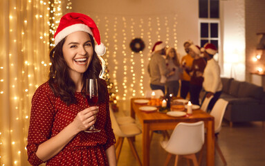 Portrait of smiling young Caucasian woman in Santa hat and champagne celebrate New Year winter holiday with friends indoors. Happy female cheers greeting congratulating with Christmas.