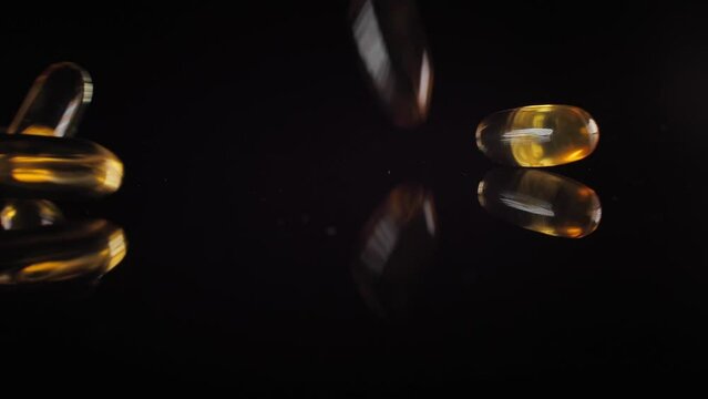 Fish oil in capsules falls on the black mirror. Capsules with vitamins