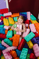 Child of preschool age playing with plastic constructor construction bricks sitting in kindergarten. Little girl playing with colorful big blocks in the playroom. Entertainment center for children.