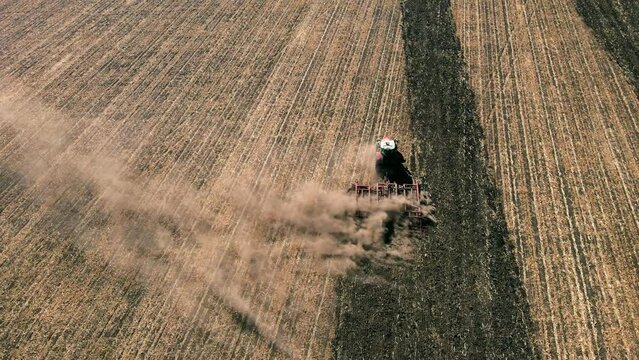 Farmer tractor plowing the dusty arid soil, aerial follow shot