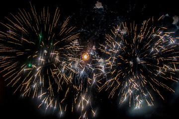 beige and yellow fireworks burst into various shapes in the dark sky during the holiday