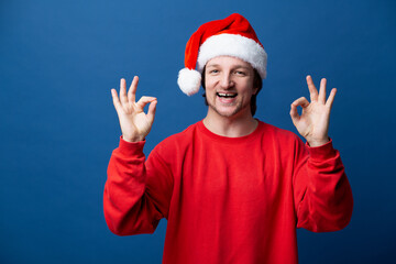 Man in Santa Claus hat smiling and shows 