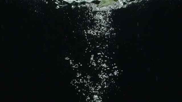 Close- up of an eggplant  falling into the water against a black background in a slow motion.
