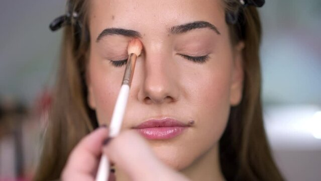 The professional make up artist putting nude eyeshadow on eyelid of a woman.