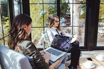 Woman using laptop computer while colleague reading book in cafe