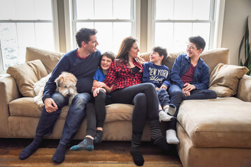 Happy family of five sitting closely on couch together with dog.