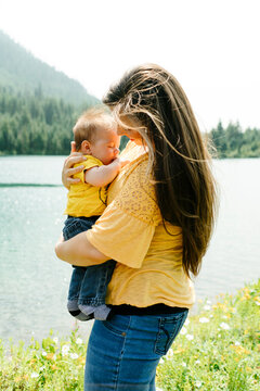 Side view of a mother holding her baby son by a mountain lake