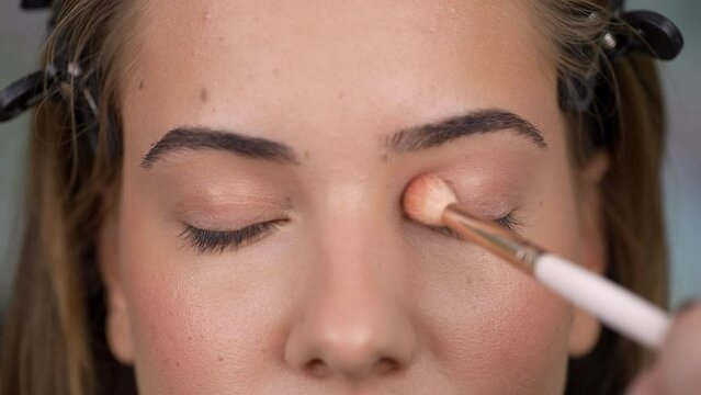 Close up of make up artist's hand, applying eyeshadow to young woman's eye using brush.