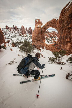 A skier makes a turn in front of a natural rock arch in the desert.