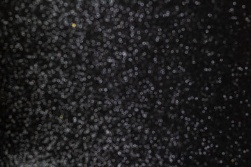 Fundo preto natalino cheio de brilhos de gliter. Fundo preto com brilhos desfocados.