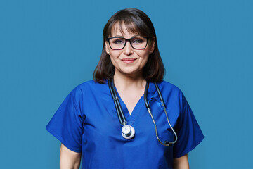 Middle aged female nurse in blue uniform with stethoscope smiling looking at camera