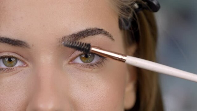 Close up of make up artist's hand combing and styling the eyebrows of young woman with a brush.�