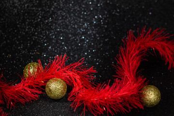 Guirlanda vermelha com alguns bolas de Natal douradas em um fundo preto com brilhos.
