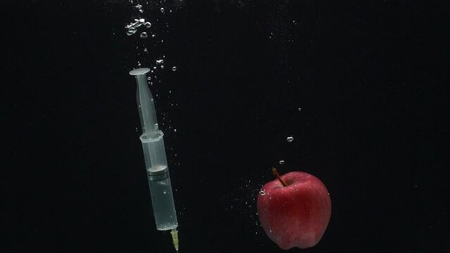 Close-up of a syringe and an apple falling into the water against a black background in a slow motion. Drug temptation.