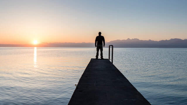 Lonely man standing on pier by Geneva Lake, at sunrise in summer, Gland, Vaud, Switzerland