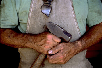 The Grimmy hands of a blacksmith holding a well used hammer.