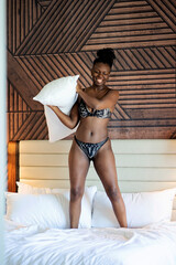 Black woman jumping on bed with pillow