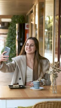 Young woman taking a selfie with a coffee and a cake before eating it in cafe.