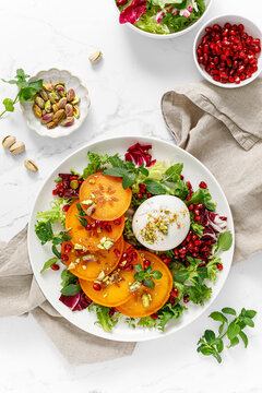 Salad with persimmon, burrata, pomegranate and pistachio, healthy food, top view