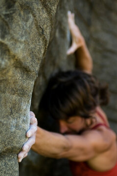 A young woman rock climber concentrates on the smooth, almost featureless rock of a limestone boulder in Waitomo, New Zealand.