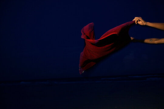 A woman in a bikini waves a red towel on the beach near the ocean at dusk.
