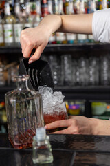 Woman bartender pouring crushed ice into glass on bar counter using a special scoop.