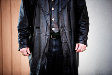 Cropped front view of a man wearing a long black leather jacket.