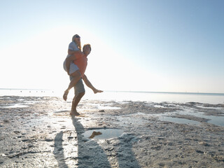 Couple piggyback along beach