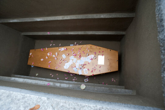 A coffin lays at the bottom of a grave with flower petals and paying cards
