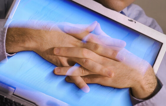 Blurred image of hands clasped tightly around a compuer screen.