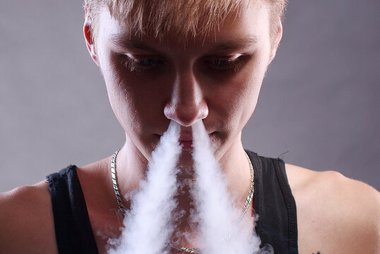 Young man white smoke nose over grey background