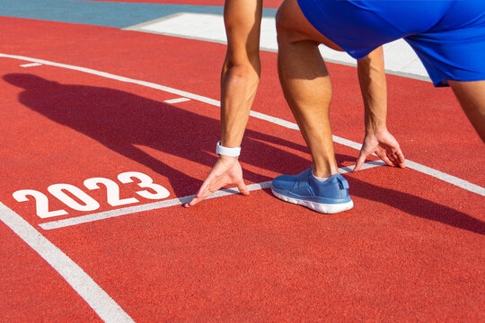 Start A New Year. Athlete Man Starts In Line For The Race At The Start With The Number 2023 On The Cross Country Ready For A Quick Sprint, Field With Sunlight. Easy Start Concept Win Victories.