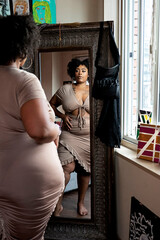 Black woman wearing brown dress looking in the mirror