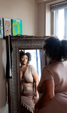 Black woman wearing brown dress looking in the mirror