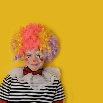 A boy in a clown costume on the background of a bright yellow wall is fooling around and smiling