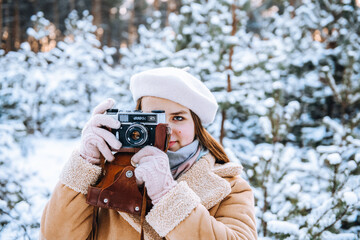 Portrait of cute smiling caucasian teenage girl taking photo with retro camera in winter snowy...