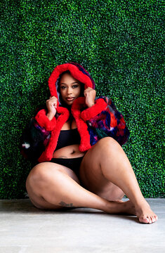 Plus size Black woman sitting in front of grass wall with coat bra and panty on