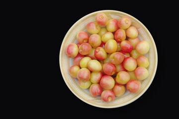 Fresh pink cherries in a plate on a black background. View from above. Close-up.