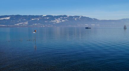 empty harbour of Lindau island on tranquil lake Constance or lake Bodensee with the Austrian Alps in the background on a fine winter evening with blue sky reflected in the water (Germany)